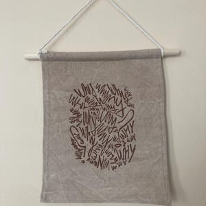 May include: A beige canvas banner with a brown graphic of the word "why" repeated in a circular pattern.
