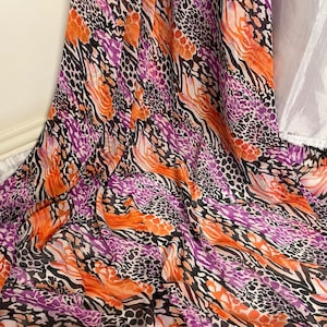Puede incluir: Una tela colorida con un estampado de animales en morado, naranja y negro. La tela tiene una textura ligera y transparente.