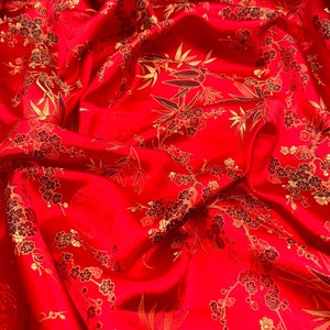Puede incluir: Tela roja con un patrón floral dorado y negro. La tela tiene un brillo sedoso y es perfecta para proyectos de artesanía o costura.
