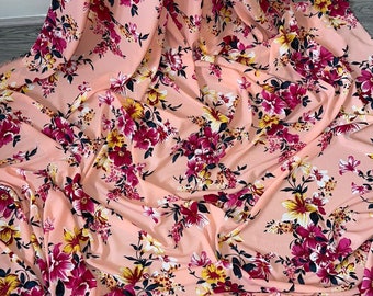 Puede incluir: Tela de color melocotón con estampado floral con flores rosas, amarillas y blancas. La tela tiene una textura suave y fluida.
