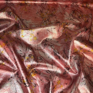 Puede incluir: Tela rosa con un estampado floral. La tela tiene una calidad brillante e iridiscente. El diseño floral incluye flores amarillas y blancas con tallos y hojas negras. La tela está arrugada y doblada, creando sombras y reflejos.