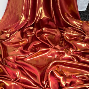 Peut inclure: Gros plan sur un tissu métallique avec une finition chatoyante dorée et rouge. Le tissu est drapé et plié, créant un aspect luxueux et élégant.