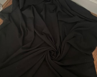 May include: A large piece of black fabric, possibly a textile or cloth, is draped and swirled, creating folds and shadows. The fabric appears to be a solid color, with a matte finish. The edges of the fabric are visible, suggesting it may be a cut piece.