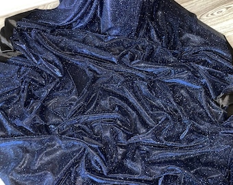 Op de afbeelding: Een close-up van een donkerblauwe stof met een glinsterende afwerking. De stof is gedrapeerd en gevouwen, waardoor de textuur en glans zichtbaar zijn.