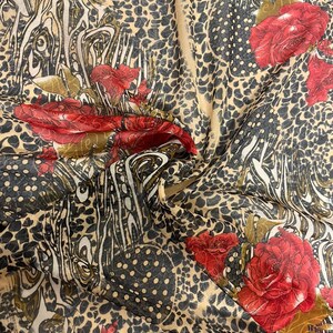 Puede incluir: Una tela transparente con un fondo beige y un estampado de leopardo. La tela está decorada con rosas rojas y lunares negros.