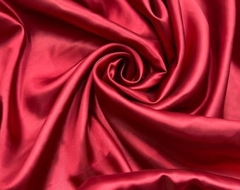 May include: Close-up of a deep red satin fabric with soft, flowing folds and a swirling pattern.