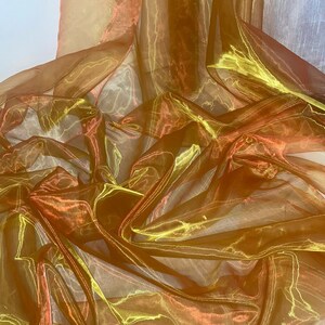 May include: A sheer fabric with a shimmering gold and orange iridescent finish. The fabric is draped and folded, showcasing its texture and drape.