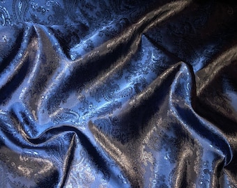 Könnte beinhalten: Blauer Stoff mit Paisley-Muster und Satin-Finish. Der Stoff ist drapiert und gefaltet, wodurch die Textur und der Glanz sichtbar werden.