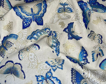 Könnte beinhalten: Weißer Stoff mit einem sich wiederholenden Muster aus blauen und goldenen Schmetterlingen. Die Schmetterlinge sind stilisiert und haben einen metallischen Glanz.