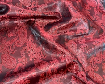 May include: Red paisley patterned fabric with a satin sheen. The fabric is folded and draped, showing the texture and pattern.