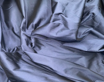 May include: A close-up of a smooth, dark blue fabric with a silky texture. The fabric is draped and folded, creating soft, flowing lines.