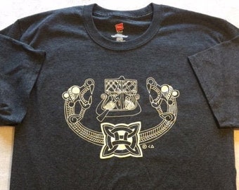 May include: Dark gray t-shirt with a crew neck and short sleeves. The shirt features a cream-colored graphic design of a Celtic knot and stylized animal heads. The design is centered on the front of the shirt.