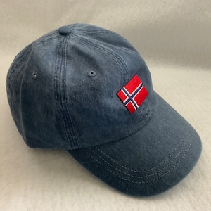 May include: A dark blue denim baseball cap with a small embroidered Norwegian flag on the front.