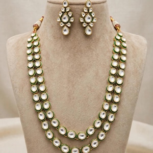 May include: A two-layer necklace and matching pair of earrings featuring white teardrop and oval stones set in gold-toned metal with green enamel borders. The necklace has two strands of oval stones, and the earrings feature a teardrop-shaped design.