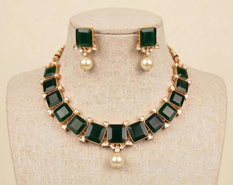 May include: A jewellery set consisting of a necklace and matching earrings. The necklace features square-cut dark green stones set in gold-tone metal, accented with small white stones and a single central cream-coloured pearl drop pendant.