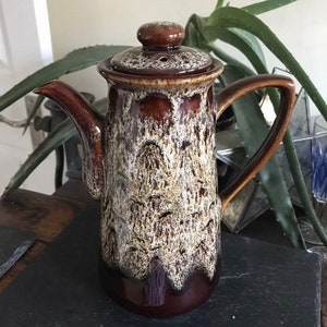May include: A brown and white ceramic coffee pot with a lid. The pot has a mottled glaze with brown and white swirls.