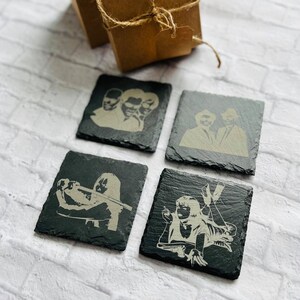 May include: Set of four black slate coasters featuring white silhouettes of characters from the movie Pulp Fiction. The coasters are square shaped and have rounded corners.