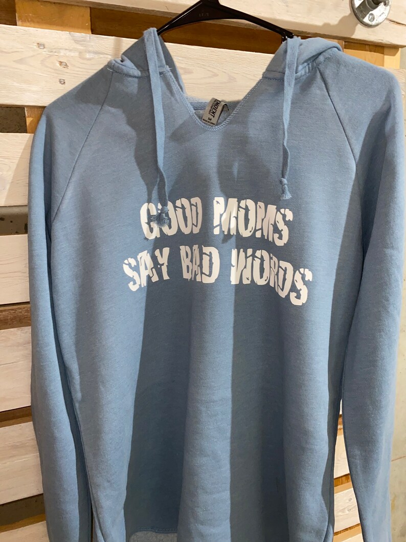 Op de afbeelding: Een lichtblauw hoodie met de tekst "Good Moms Say Bad Words" in wit gedrukt.