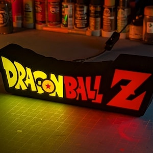 May include: A black light-up sign with the words "Dragon Ball Z" in yellow, red, and white. The sign is lit up with yellow and red lights.