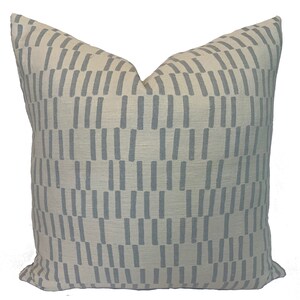 May include: Square decorative pillow with a cream-colored background and a repeating pattern of vertical, light blue rectangles. The pillow has a soft, textured appearance, suitable for home decor.