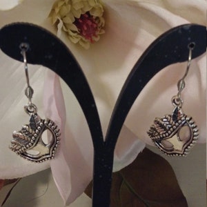 Op de afbeelding: Een paar zilveren oorbellen met een hartvormig ontwerp met een boom met bladeren. De oorbellen hangen aan een zwarte oorbellenstandaard.