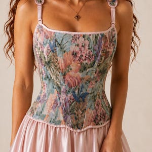 May include: A corset top featuring a multi-colored floral tapestry pattern in shades of pink, blue, and green with a sweetheart neckline and adjustable shoulder straps, paired with a solid light pink satin skirt with a gathered waistline.