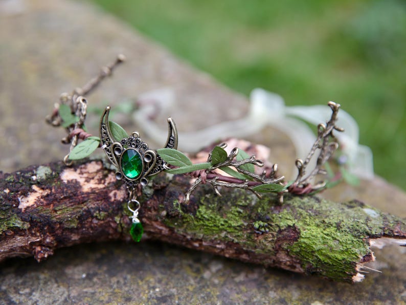 Fairy crown, elven tiara, green foliage, the centre is decorated with a metal crescent moon and green hanging crystal. Adjustable at back with a ribbon tie.