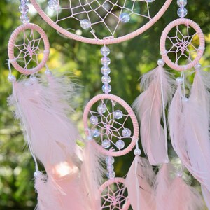 Pretty Pink coloured dream catcher with 5 circles decorated with beads and large hanging pink feathers.