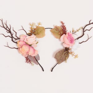Puede incluir: Dos diademas decorativas con forma de cuernos de ciervo. Cada diadema presenta cuernos marrones, rosas rosas y melocot&oacute;n, y hojas verdes y marrones. Las diademas est&aacute;n sobre un fondo blanco.