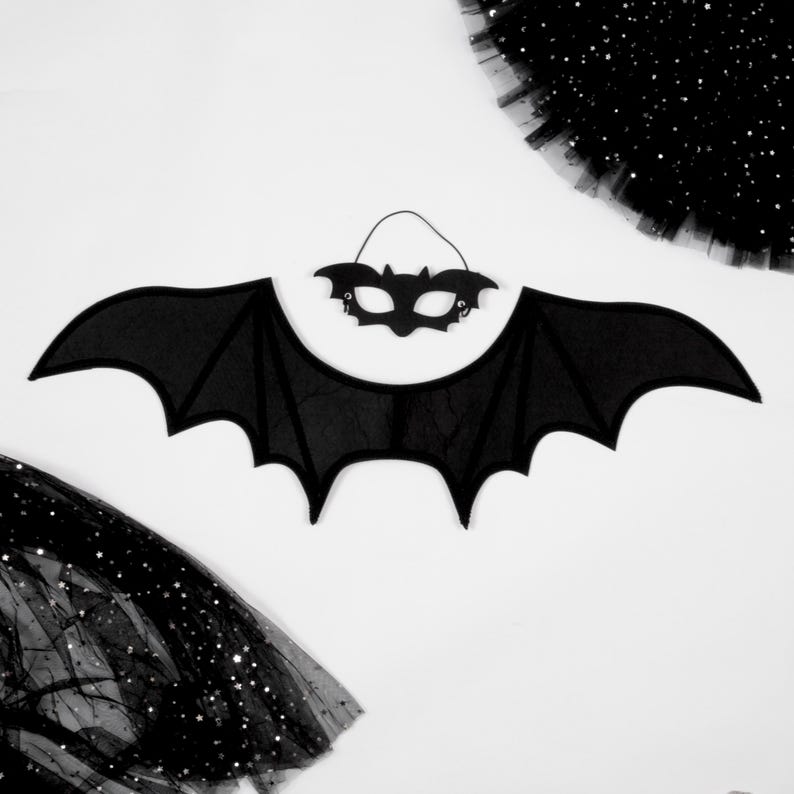 May include: A black bat wing costume accessory with a matching black bat-shaped eye mask. The wings feature a pointed, scalloped edge design, and the mask includes a thin elastic strap for securing it in place against the face.