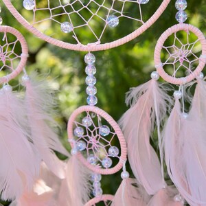 Pretty Pink coloured dream catcher with 5 circles decorated with beads and large hanging pink feathers.
