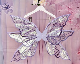 May include: Purple iridescent fairy wings with glitter and a delicate design. The wings are attached to a white hanger.
