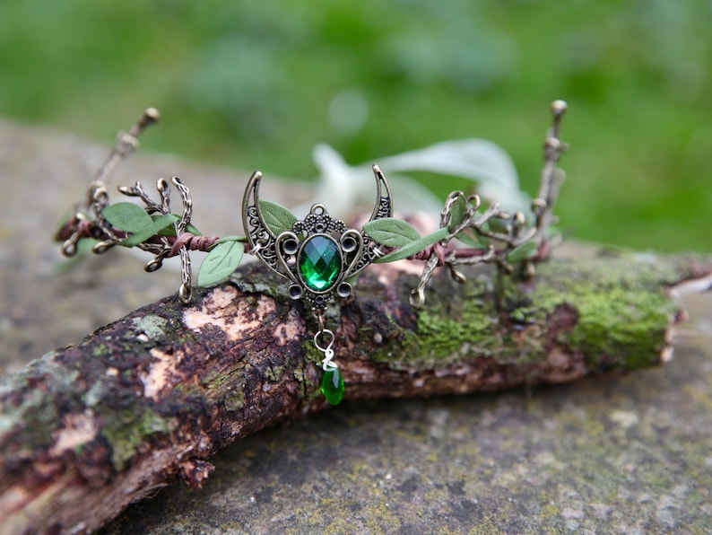 Fairy crown, elven tiara, green foliage, the centre is decorated with a metal crescent moon and green hanging crystal. Adjustable at back with a ribbon tie.