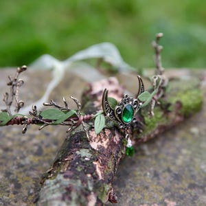 Fairy crown, elven tiara, green foliage, the centre is decorated with a metal crescent moon and green hanging crystal. Adjustable at back with a ribbon tie.