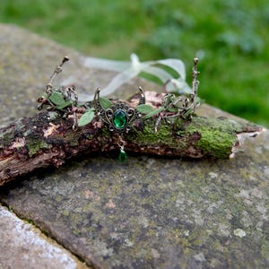 Fairy crown, elven tiara, green foliage, the centre is decorated with a metal crescent moon and green hanging crystal. Adjustable at back with a ribbon tie.