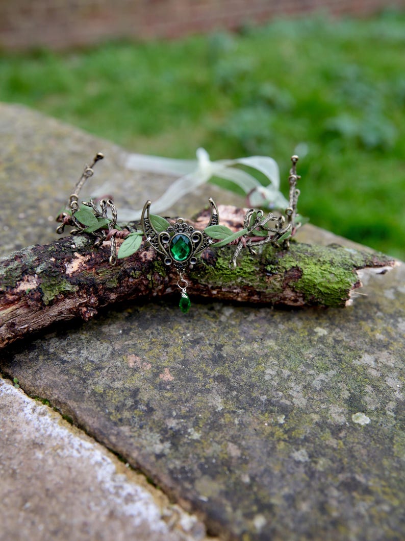 Fairy crown, elven tiara, green foliage, the centre is decorated with a metal crescent moon and green hanging crystal. Adjustable at back with a ribbon tie.