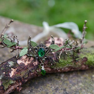 Fairy crown, elven tiara, green foliage, the centre is decorated with a metal crescent moon and green hanging crystal. Adjustable at back with a ribbon tie.