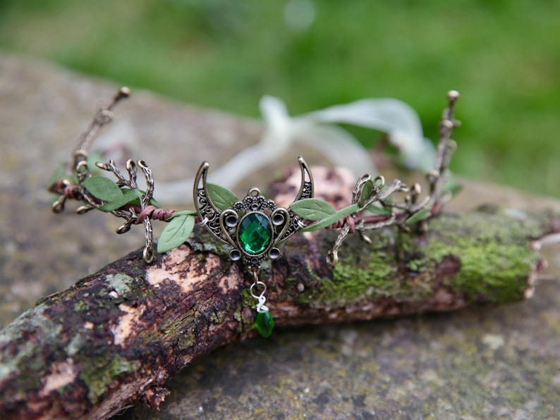 Fairy crown, elven tiara, green foliage, the centre is decorated with a metal crescent moon and green hanging crystal. Adjustable at back with a ribbon tie.