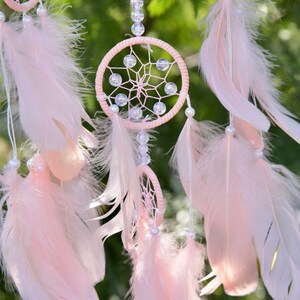 Pretty Pink coloured dream catcher with 5 circles decorated with beads and large hanging pink feathers.