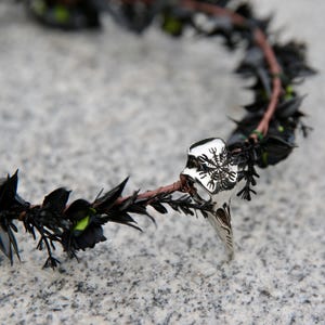 May include: A black floral crown with a silver pendant featuring a snowflake design.