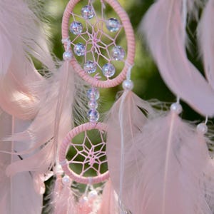 Pretty Pink coloured dream catcher with 5 circles decorated with beads and large hanging pink feathers.