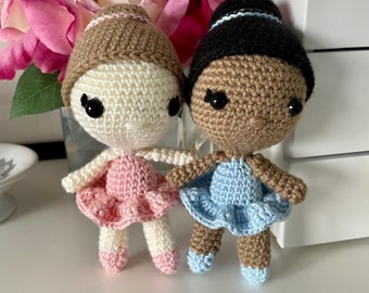 May include: Two crocheted ballerina dolls, one with a pink tutu and the other with a blue tutu. The dolls have brown hair and are wearing white ballet shoes. The dolls are standing on a white surface. Mini Bella Ballerina Crochet Pattern SheffStudios