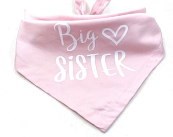 May include: Pink fabric bandana with white text that says "Big Sister" with a heart symbol.