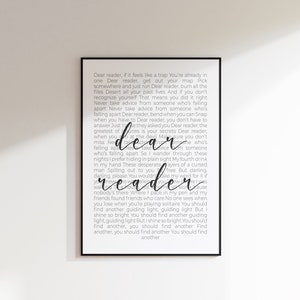 以下が含まれることがあります： 「Dear reader」の文字が筆記体で書かれた、印刷されたテキストを背景にした額入りのアートプリント。白の背景と黒のテキストを使用したミニマリストなデザインです。