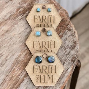Peut inclure: Trois paires de boucles d'oreilles en labradorite bleu irisé sur des cartes d'affichage en bois hexagonales avec le texte "Earth and Elm" imprimé sur chaque carte.
