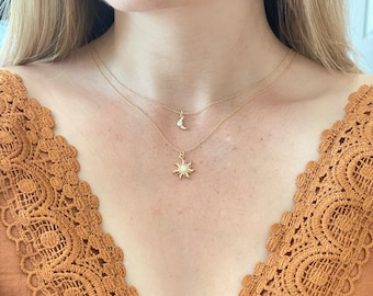 May include: A woman wearing a brown lace top with a gold chain necklace featuring a sun and moon pendant.