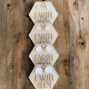 Può includere: Quattro paia di orecchini a perno in cristallo rosa esposti su carte di legno esagonali con il testo "Earth and Elm" stampato su ogni carta.