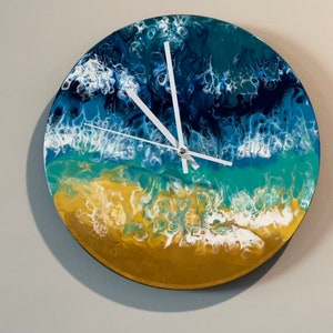 May include: A round clock with a white face and white hands. The clock face is painted with a blue, green, and gold abstract design that resembles an ocean scene.