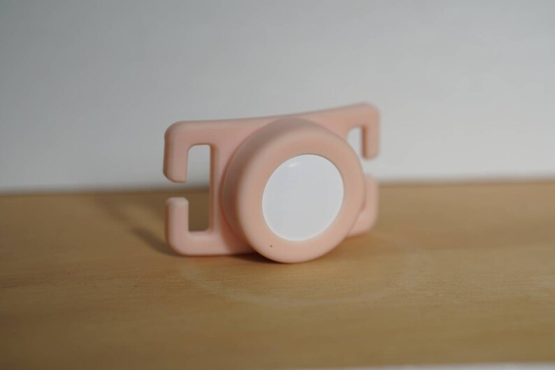 May include: A pink plastic safety strap with a white button in the center. The strap has two loops on either side.