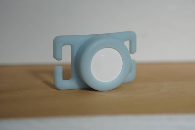 May include: A light blue plastic baby teether with a white circle in the center.